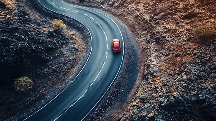 Fototapeta premium Red Car Driving on Winding Mountain Road Through Dramatic Rocky Landscape