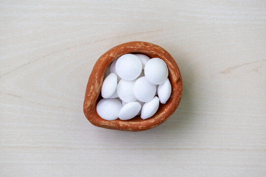 An earthen pot full of white naphthalene balls on wooden background. Top view.