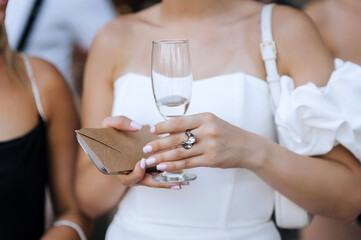 Woman, a guest invited to the celebration, holds a glass of champagne and an envelope with a cash gift at the ceremony. Wedding photography, portrait.