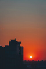 Obraz premium A stunning sunset paints the sky as the sun descends into clouds with a distant building in the foreground. The scene captures the beauty of urban and natural elements harmoniously blending at dusk.
