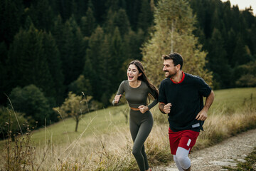 Fototapeta premium A young man and woman in sportswear talking and laughing while running together in a park