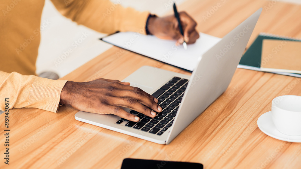 Poster copywriter. close up afro businessman writing content on notebook, using laptop at wooden table at o