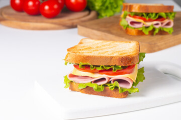 Close-up of two sandwiches with bacon, salami, prosciutto and fresh vegetables on rustic wooden cutting board. Club sandwich concept