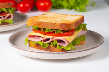 Close-up of two sandwiches with bacon, salami, prosciutto and fresh vegetables on rustic wooden cutting board. Club sandwich concept