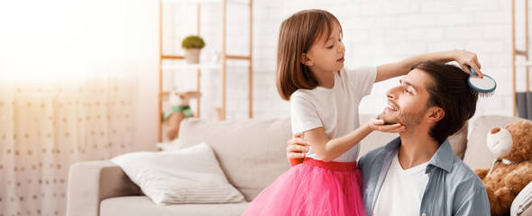 Fototapeta premium Little cute girl brushing father hair, daughter making daddy look good, home interior