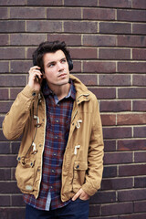 Headphones, man and listening to audio on brick wall background for relax, podcast or hearing radio. Music, sound and person in city for streaming hip hop, audiobook or thinking of urban song outdoor