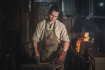 Blacksmith forges a red-hot metal piece on an anvil in a rural forge. Traditional crafts