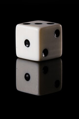 a white six-sided D6 dice with black dots, showing one dot, on a black background with a reflection