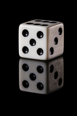 a white six-sided D6 dice with black dots, showing five dots, on a black background with a reflection