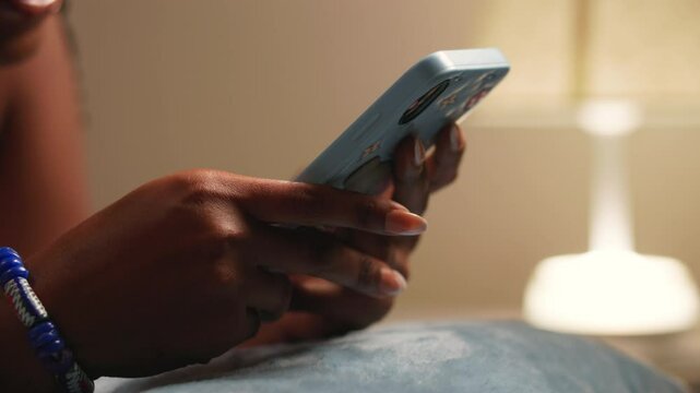 Close-up of an African woman's hands holding a smartphone, illuminated by a soft lamplight.