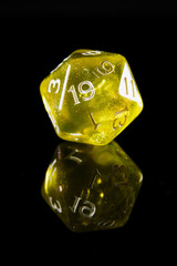 a translucent yellow twenty-sided dice with white numbers, showing the number nineteen, on a black background with a reflection