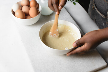 cupcake batter being mixed in a white mixing bowl, hand holding a wood spoon mixing vanilla cake batter