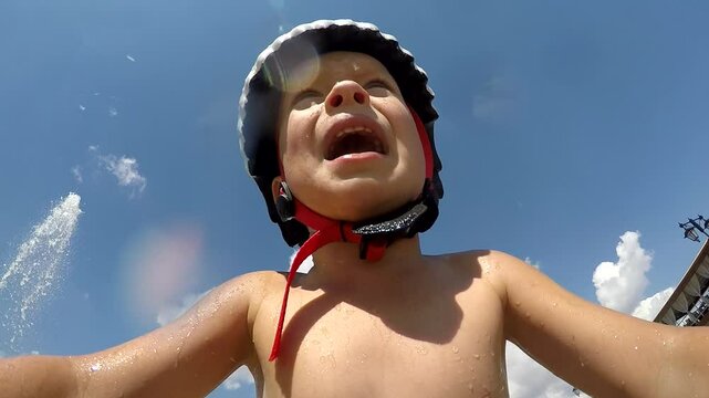 Happy wet child riding balance bike through fountain streams in summer action camera pov. Little boy bathing in fountain water. Light and music fountain on Tereshkova embankment. Yevpatoria, Crimea