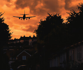 Airplane silhouette against an orange sunset sky over suburban houses. 