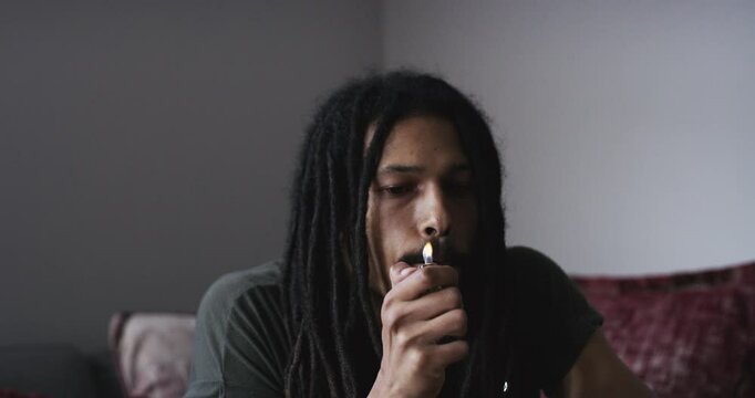 Man, weed and light cigarette in home, 420 and cannabis in living room of apartment to relax. African person smoke marijuana joint, drugs abuse and hemp paper, natural cbd plant and thc addiction