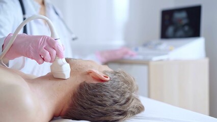 Doctor woman with pink medical gloves performing neck ultrasound exam on male patient. Thyroid...