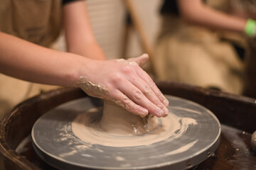 Potter girl works on potter's wheel, making ceramic pot out of clay in pottery workshop