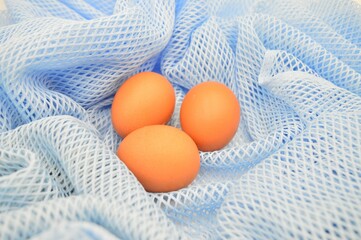 Three brown eggs resting on a light blue mesh fabric
