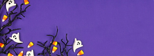 Halloween corner border of spooky black branches and candy. Top view over a purple banner background with copy space. © Jenifoto