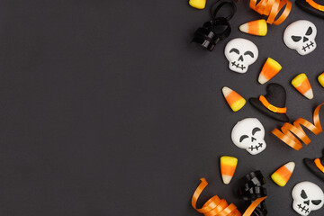 Halloween side border of black, white and orange color candy and ribbon. Overhead view on a black background with copy space.