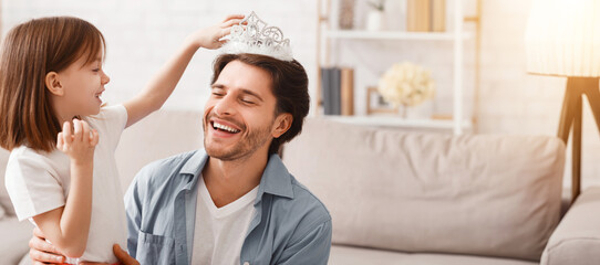 Obraz premium Little daughter putting crown on her laughing dad head, having fun together at home, princess day, close up