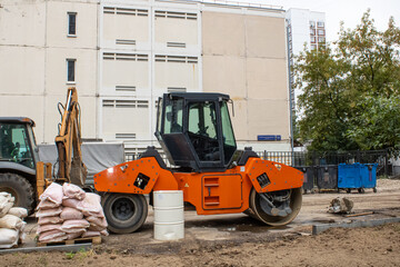 An orange road roller, a large vehicle, is parked in front of a building