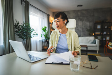 Fototapeta premium Mature japanese woman with earphones work from home on laptop