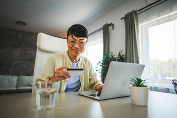 mature happy japanese woman buy online on laptop with credit card