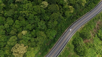 Aerial view of a road in the middle of the forest. Top view of asphalt road through forest with car adventure. Healthy environment road trip travel.
