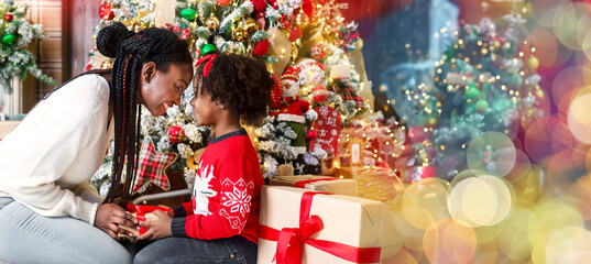 Christmas gift from mom. Loving afro mother giving present to her little daughter, sitting under...