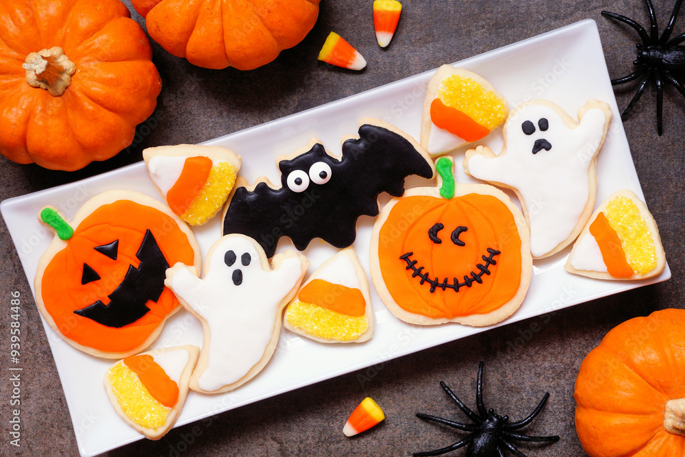 Poster plate with an assortment of spooky halloween cookies. top view with pumpkin decor on a dark table ba
