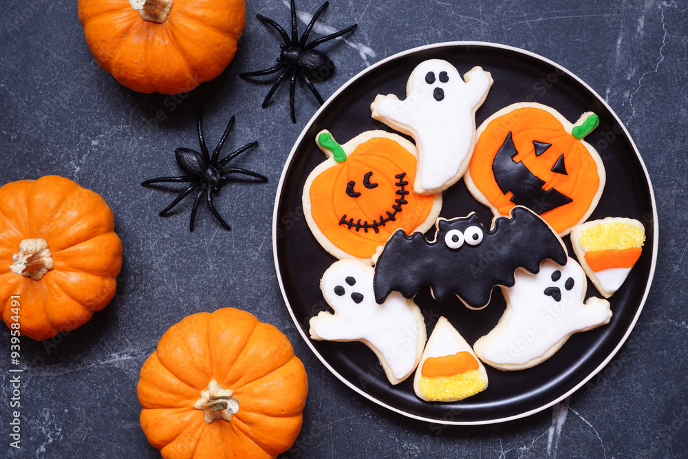 Poster plate with a variety of spooky halloween cookies. above view with pumpkin decor on a dark table back