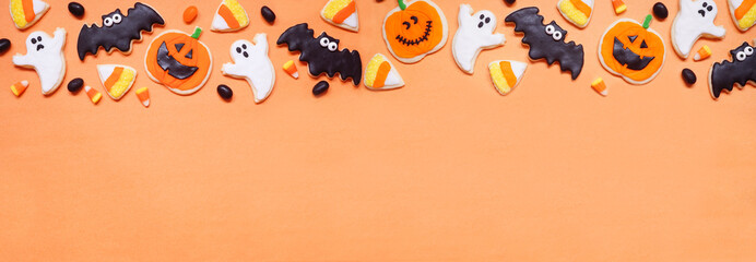 Halloween cookie top border. Overhead view on an orange banner background with copy space. Ghosts,...