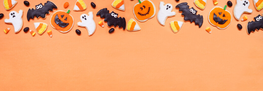 Halloween cookie top border. Overhead view on an orange banner background with copy space. Ghosts, bats, jack o lanterns and candy corn.