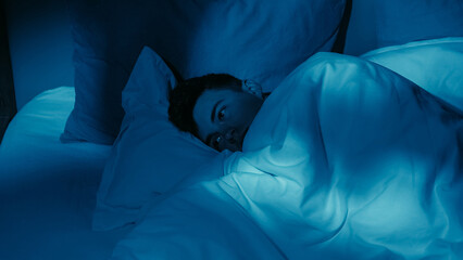 Adult male experiencing insomnia feeling alone and restless in bed trying to sleep at night.