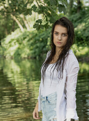 Beautiful girl with wet long hair is posing in the river. Vertically. 