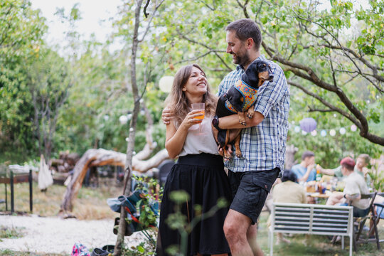 Young attractive romantic happy Caucasian couple with their pet dachshund dog spending time together during a garden party. Love and friendship concept