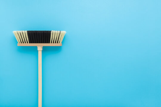 New white black broom with wooden stick on light blue table background. Pastel color. Closeup. Cleaning tool. Empty place for text. Top down view.