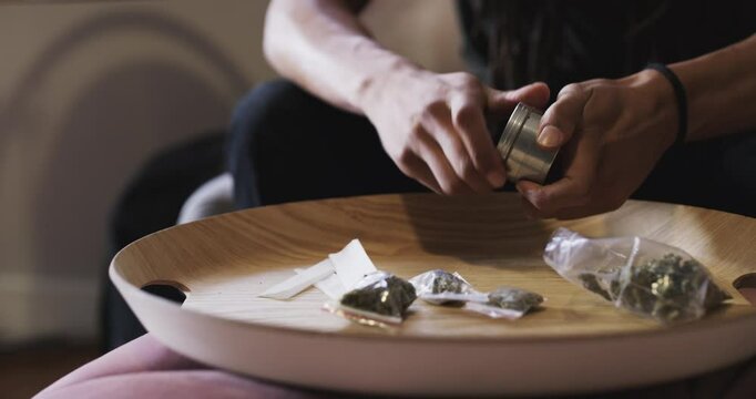 Hands, weed grinder and man at table in home, 420 and medical cannabis preparation. Closeup, person and shred marijuana herb, drugs abuse and hemp paper, natural cbd plant or thc addiction in house