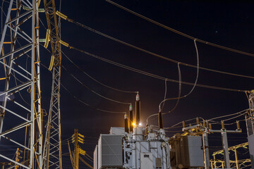 High voltage electrical transformer at power distribution station at night with industrial lighting.