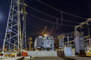 High voltage tower connected by cables to electrical substation at night with beautiful views and bright moon, view of transformer against moon and industrial lighting.