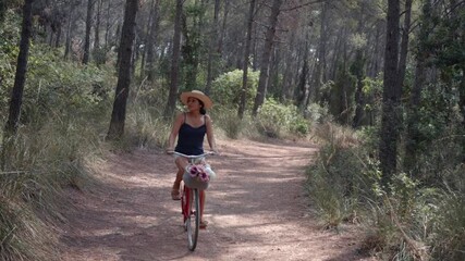 A woman rides her vintage red bicycle along a forest path.