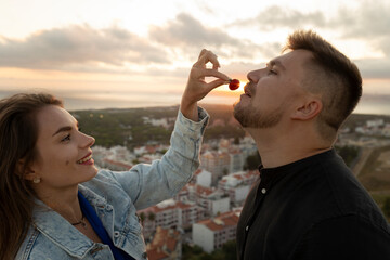 Obraz premium Young woman feeding strawberry to man at sunset with cityscape in background
