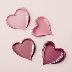 Four heart-shaped swatches of lip gloss in shades of pink and mauve on a soft pink background. Glossy textures with a romantic design.