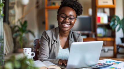 A smiling Black woman pays bills online at her home office with a laptop and calculator.
