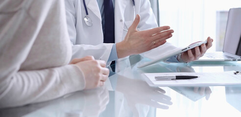 Doctor is consulting patient in modern clinic. Healthcare professional discusses medical information with a woman, using a tablet computer. Medicine concept