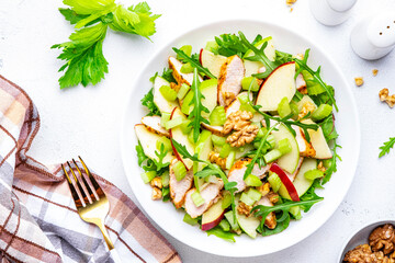 Old fashioned salad with chicken, red and green apples, raw celery, lettuce and walnuts, white background, top view