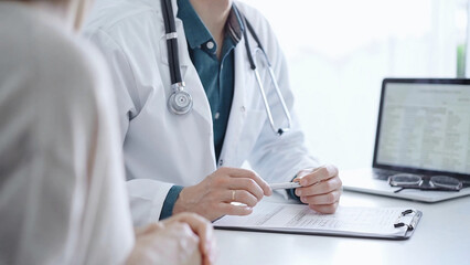 Doctor and a patient. The physician, wearing a white medical coat over a green shirt, is gesturing with his hands during a consultation in the clinic. Medicine