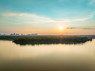 Big lake with green shores in bright sun light and city on horizon, aerial landscape. Recreation concept. Aerial view