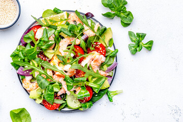 Fresh green salad with avocado, shrimps, tomatoes, arugula, lamb lettuce, onion and sesame seeds on white background. Top view